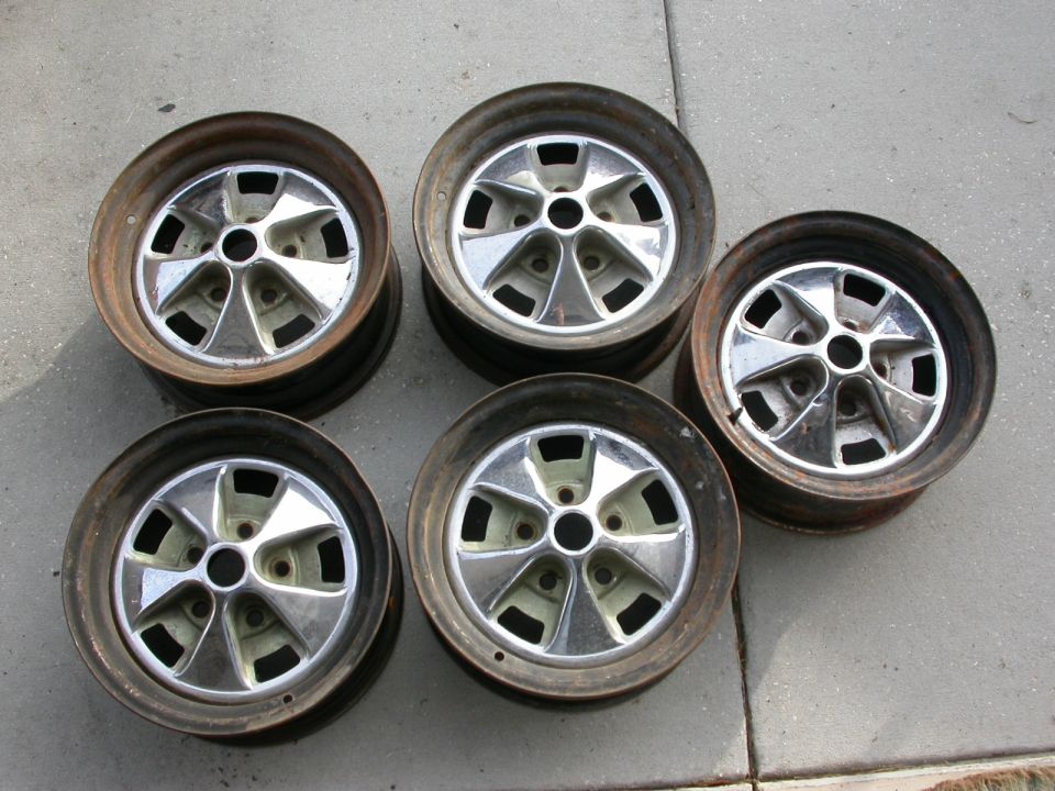 Five rusty steel wheels with chrome five-spoke hubcaps on concrete