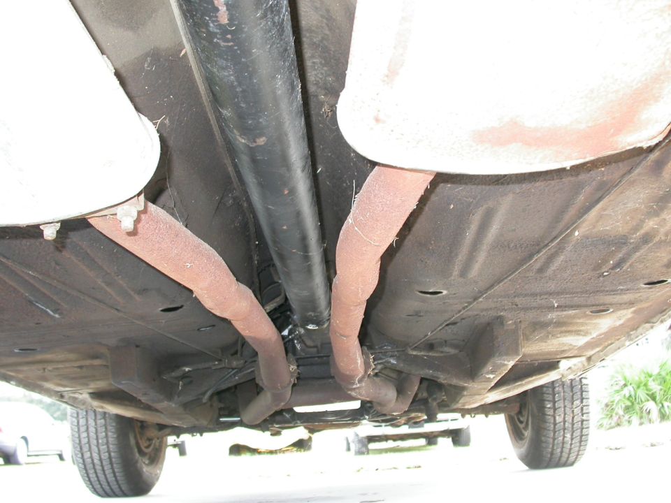 Undercarriage view showing exhaust pipes, drive shaft, and rear tire of a car