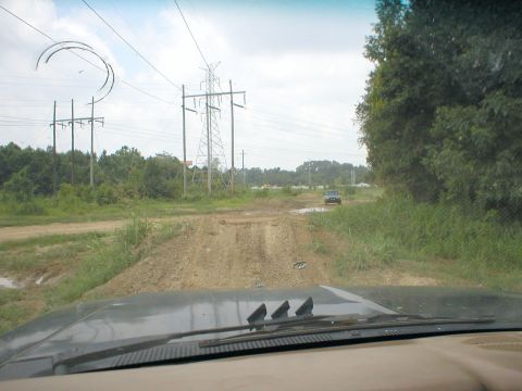 1983 Ford Bronco - A lone SUV navigates a rough, muddy track under a sky with power lines and distant trees.