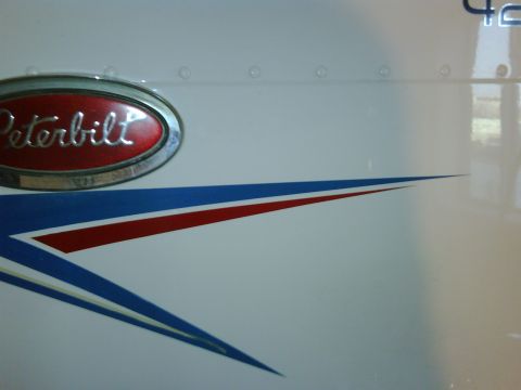 2003 Peterbilt 379 - Close-up of a Peterbilt emblem and a red and blue stripe graphic on the side of a white truck.