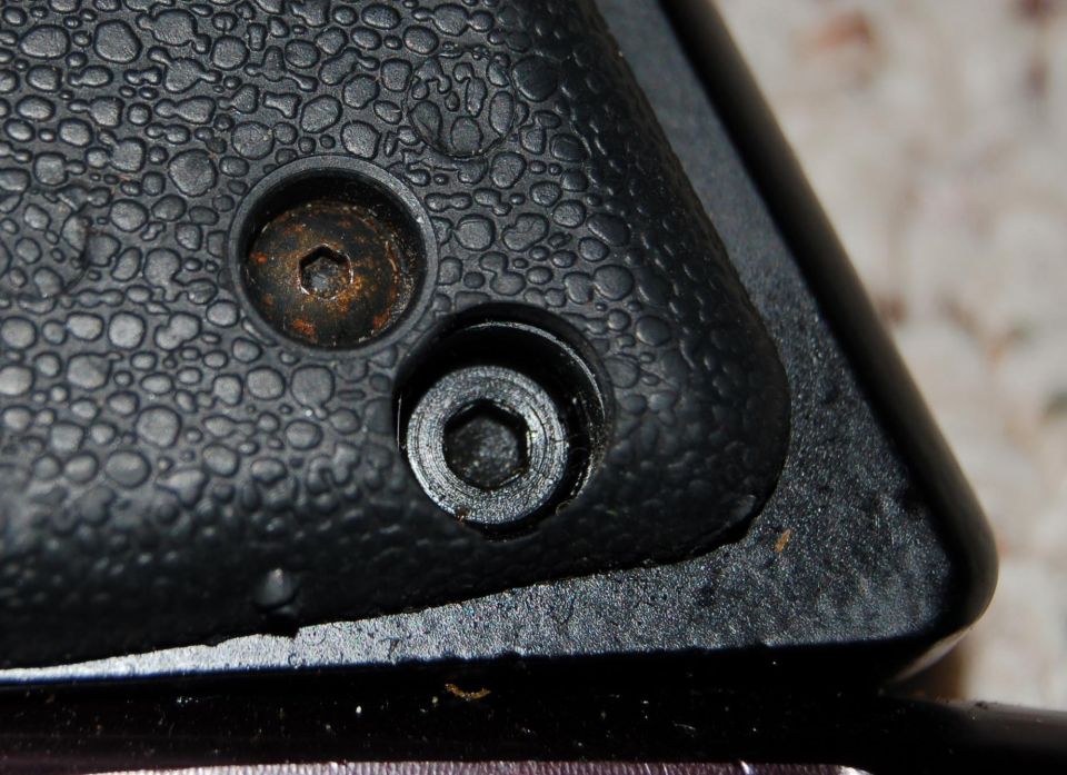 Close-up of two hex screws, one with rust, on textured black plastic