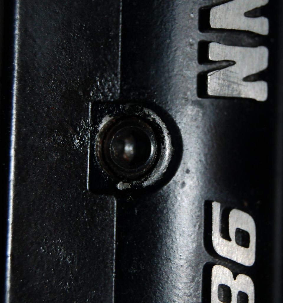 Black metal part with a bolt head and silver lettering reading "VN 96"