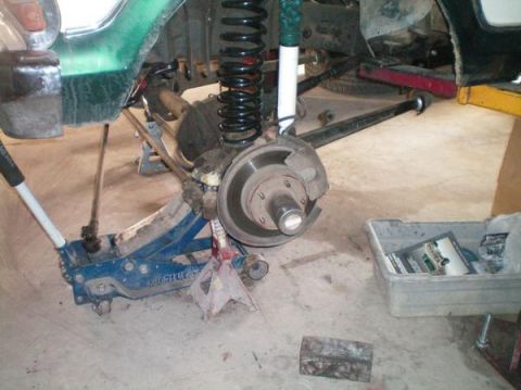 1979 Ford Bronco - The suspension and brake assembly of a green 1979 Ford Bronco is visible while it is supported by jack stands and a floor jack.
