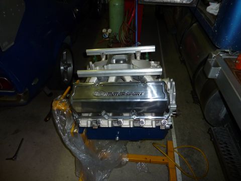 1971 Ford Mustang - Ford Motorsport engine on stand, with a blue vehicle visible in the background.