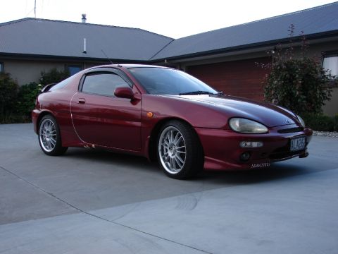 1993 Mazda MX-3 - This red coupe is parked in a driveway in front of a house.