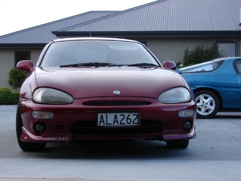 1993 Mazda MX-3 - Front view of a red 1993 Mazda MX-3 parked outside next to another car.