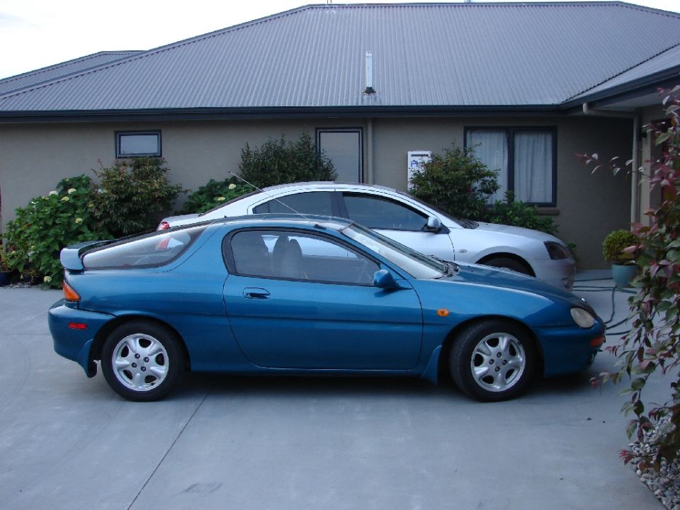 Blue 1993 Mazda MX-3 coupe parked on concrete driveway, side view