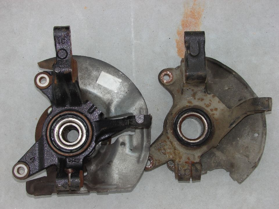 Two front wheel hubs, one black and one rusty, on a gray surface