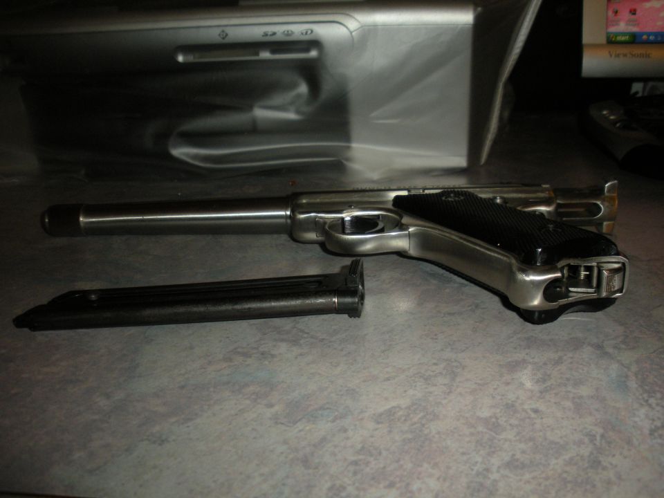 Silver handgun with black grip and detached magazine on a textured surface