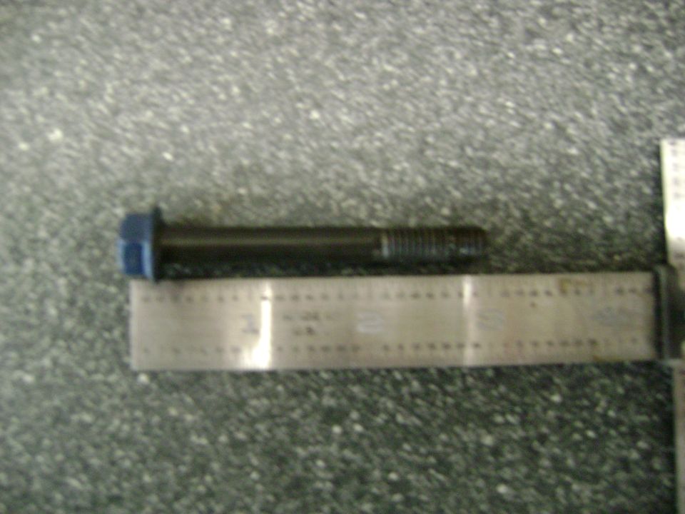Long hex-head bolt laid next to a steel ruler on a speckled surface