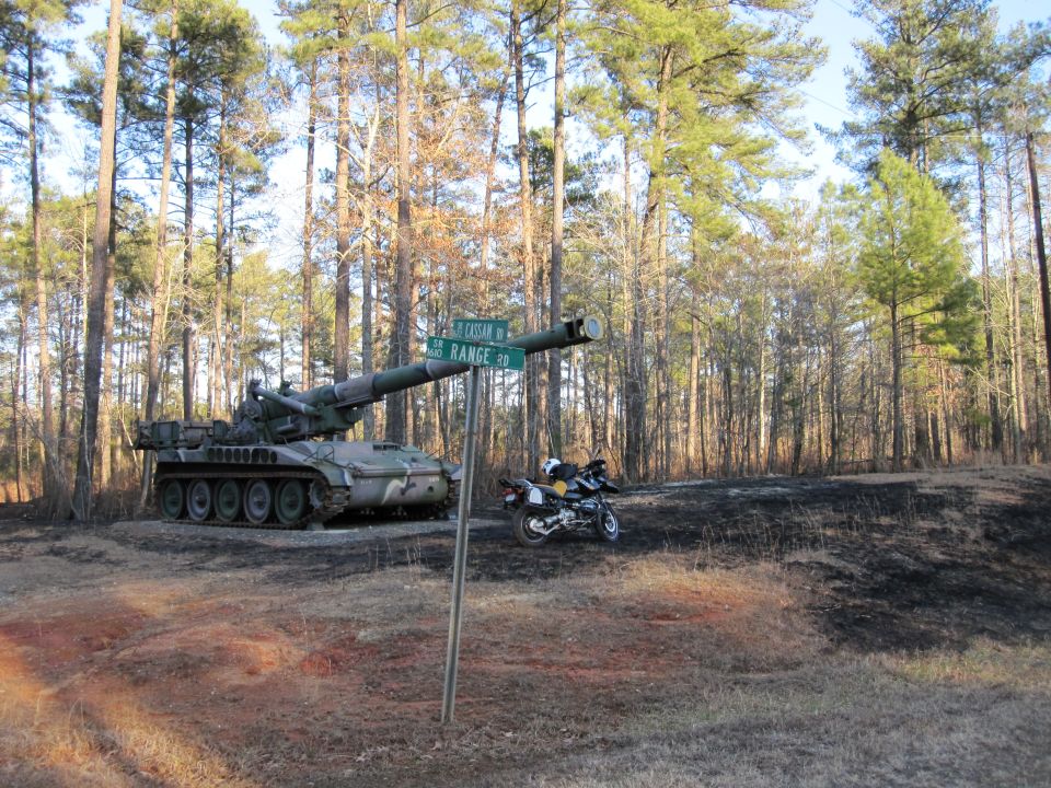 Military artillery vehicle and motorcycle behind a Range Road street sign