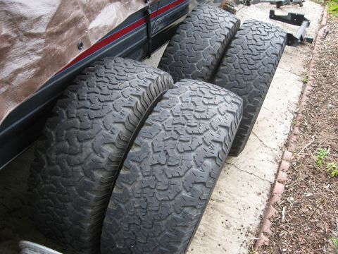 1986 Ford Bronco - Four off-road tires are shown next to a covered vehicle, with a watermark indicating the source.