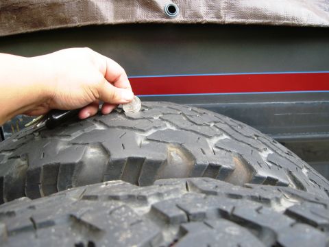 1986 Ford Bronco - A coin is used to measure the tread depth on a worn tire, with a red stripe visible on the vehicle's body.