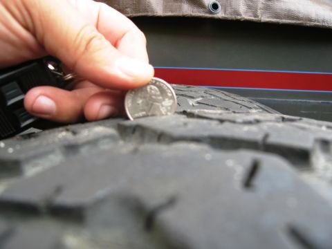 1986 Ford Bronco - A quarter is used to measure the tread depth of a tire, with a red stripe visible on the vehicle's body in the background.