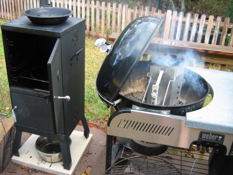 1992 Ford Bronco - A black smoker sits next to a Weber grill, both outdoors with a wooden fence in the background.