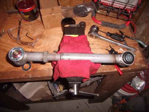 2003 Jeep Wrangler - A metal control arm is secured in a vise on a wooden workbench, surrounded by various tools and a tub of grease.