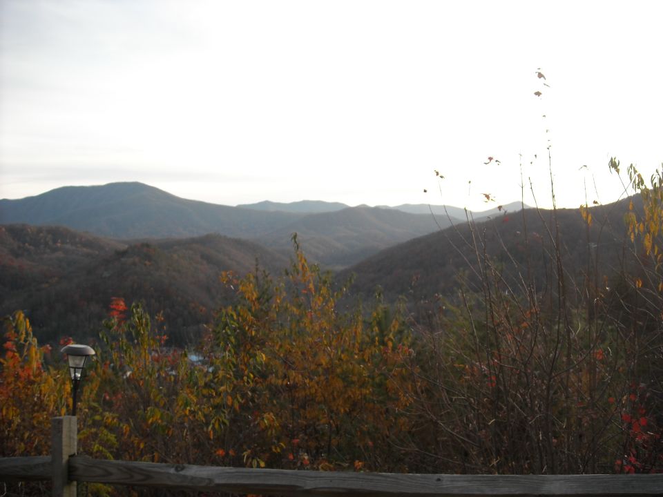Mountain range under a bright sky, with autumn foliage in the foreground and a wooden fence