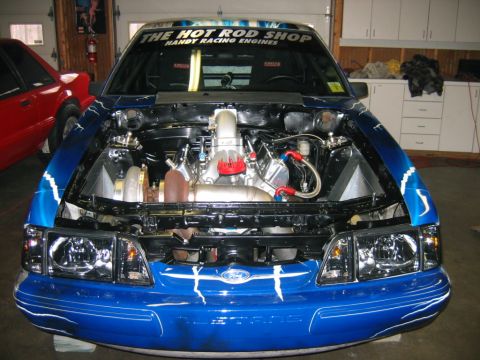 1992 Ford Mustang - A blue 1992 Ford Mustang is parked in a garage with its hood open, revealing a custom engine and racing decals.