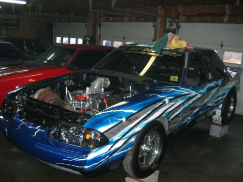 1992 Ford Mustang - A heavily modified car with a custom paint job and exposed engine sits in a garage.