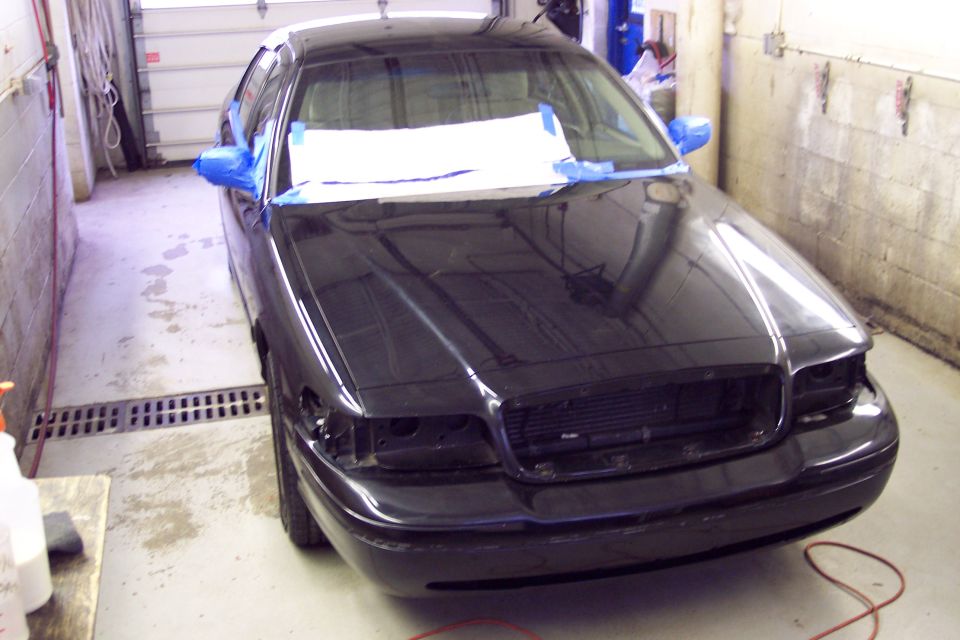 Black sedan, possibly a 2001 Ford Crown Victoria, in a garage with blue tape on mirrors and paper taped to windshield