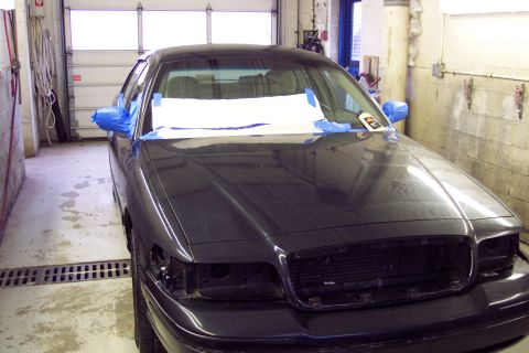 2001 Ford Crown Victoria - A dark sedan, likely a 2001 Ford Crown Victoria, is parked in a garage with its headlights removed and mirrors taped.