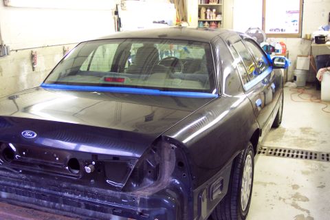 2001 Ford Crown Victoria - Rear view of a dark 2001 Ford Crown Victoria, showing blue masking tape along the trunk lid and rear quarter panel.