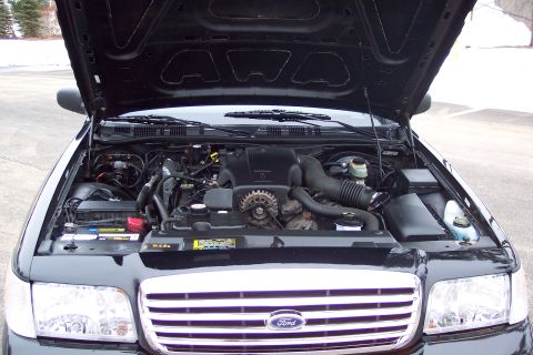 2001 Ford Crown Victoria - The engine bay of a black Ford Crown Victoria is shown with the hood open, revealing the engine and front grille.