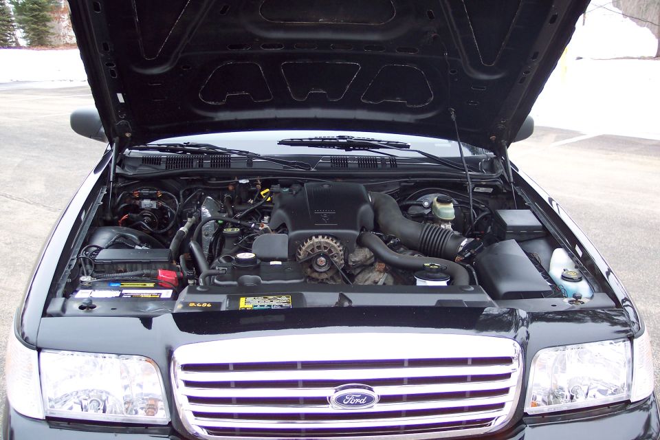 Black Ford Crown Victoria engine bay with hood open. Shows engine, battery, and grille with Ford logo