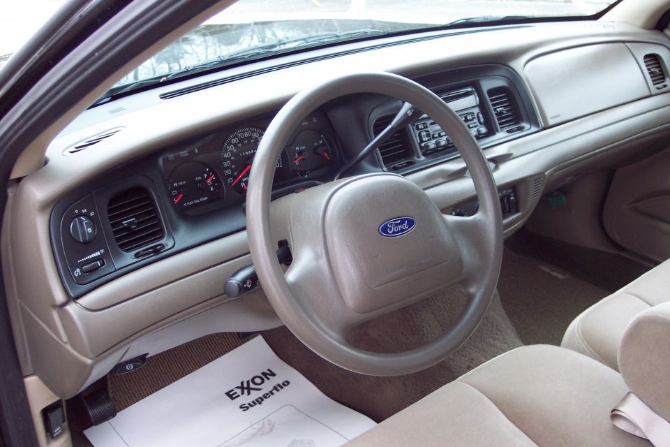 Interior view of a 2001 Ford Crown Victoria showing the dashboard, steering wheel with Ford logo, and tan seats