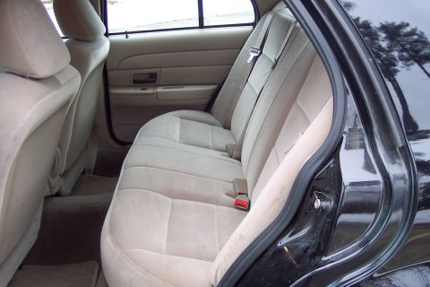 2001 Ford Crown Victoria - The interior of a car shows the rear bench seat and door frame, with a reflection of trees in the exterior paint.
