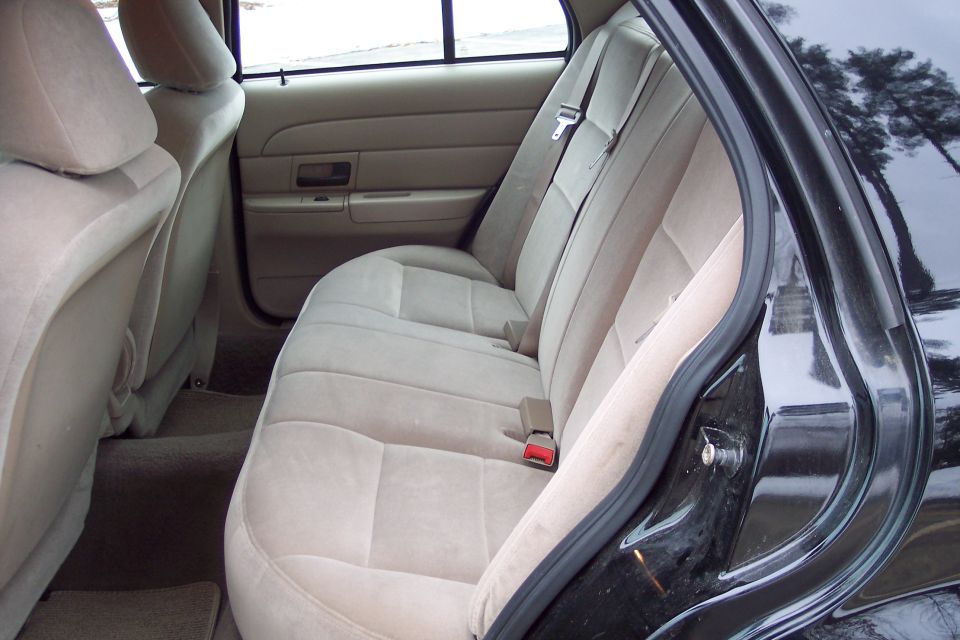 Back seat of a car, tan fabric seats, seatbelts visible. Door frame is black