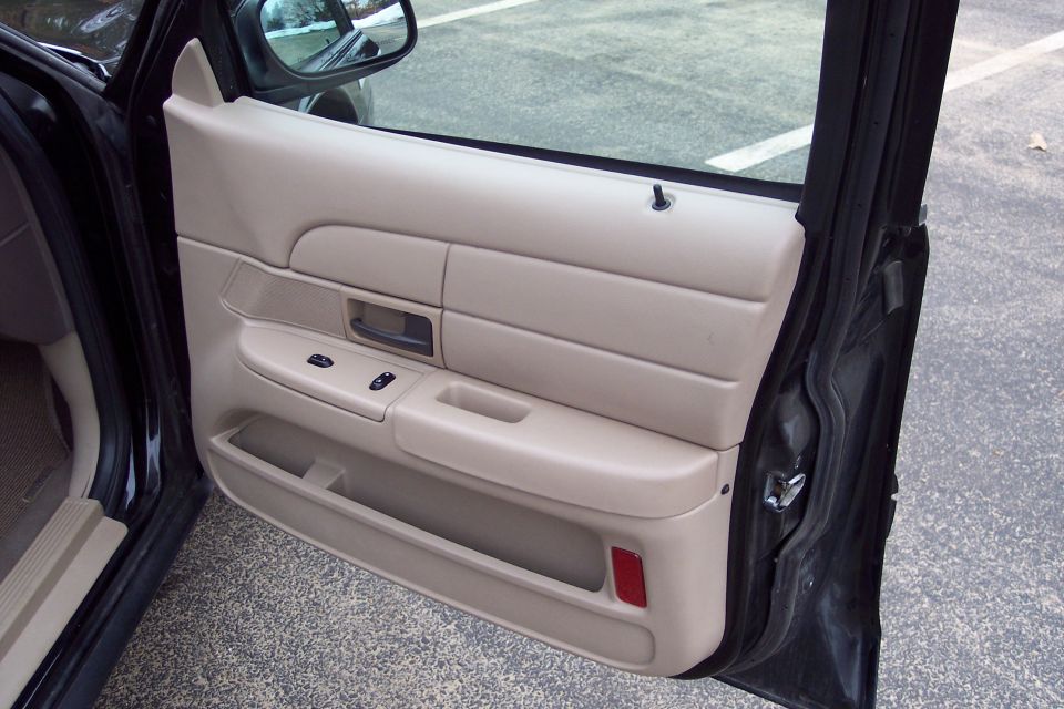Interior door panel of a car, showing tan trim, window controls, and a door handle