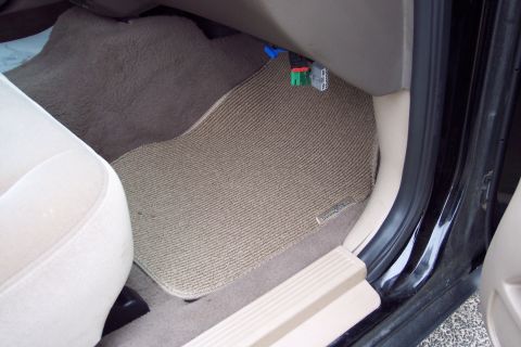 2001 Ford Crown Victoria - The interior of a car shows tan carpet floor mats and a visible wiring harness under the dashboard.