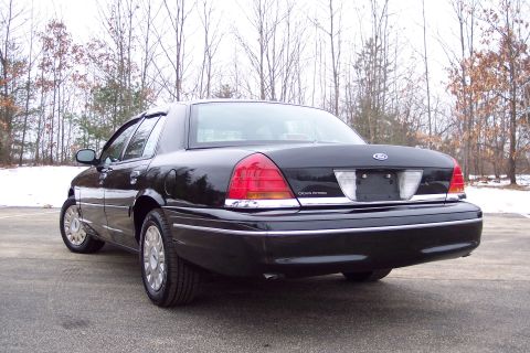 2001 Ford Crown Victoria - Rear view of a black 2001 Ford Crown Victoria parked outdoors with trees in the background.