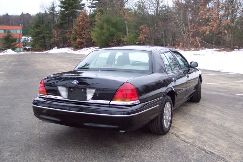 2001 Ford Crown Victoria - This black 2001 Ford Crown Victoria is parked in a lot with snow on the ground and trees in the background.