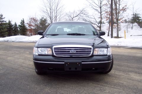 2001 Ford Crown Victoria - A black 2001 Ford Crown Victoria is shown from the front on a cloudy day with snow-covered ground and trees.
