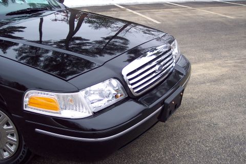2001 Ford Crown Victoria - The front of a black 2001 Ford Crown Victoria is shown from a low angle, highlighting the chrome grille and headlights.