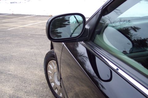2001 Ford Crown Victoria - A close-up view of the side mirror and door panel of a black sedan on a cloudy day.