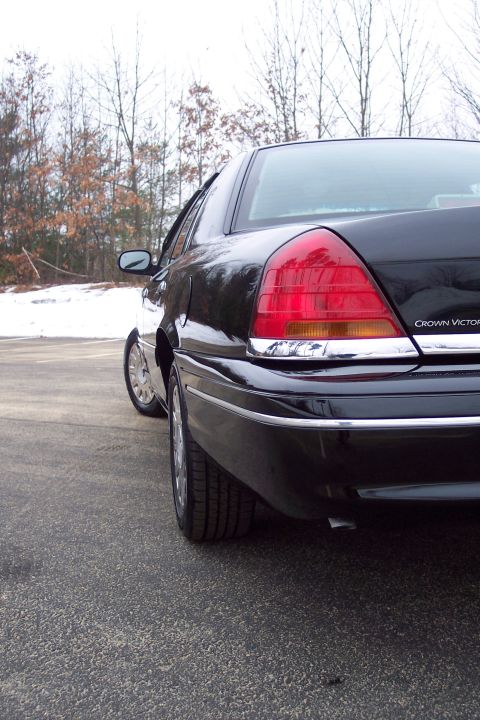 2001 Ford Crown Victoria - Rear quarter view of a black 2001 Ford Crown Victoria parked on asphalt with trees and snow in the background.