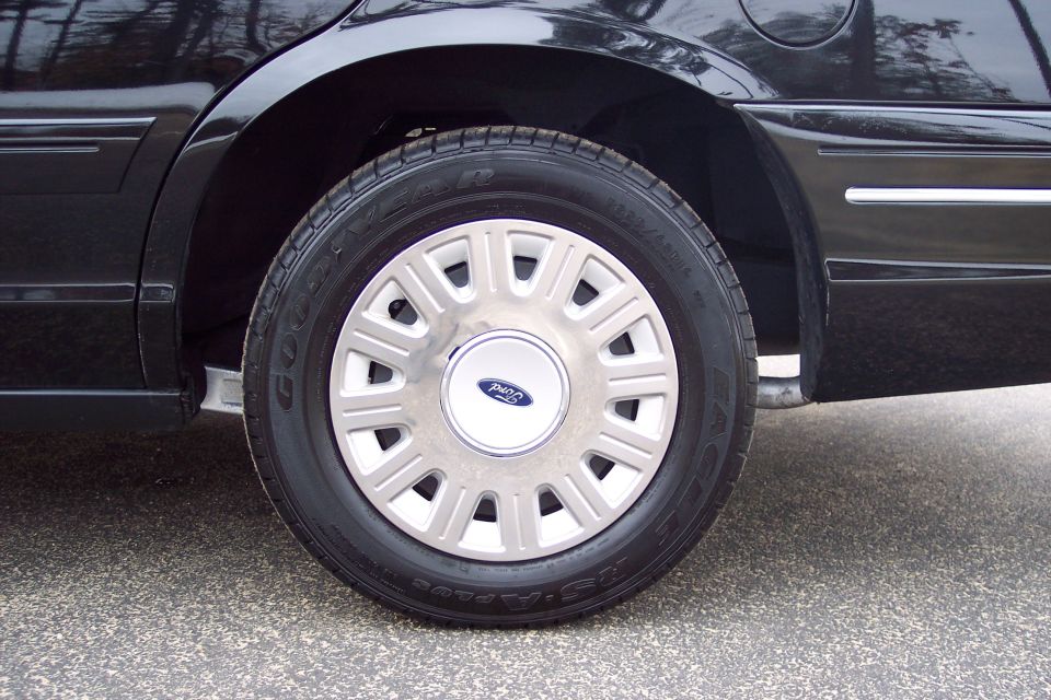 Black 2001 Ford Crown Victoria rear wheel and fender, showing a chrome hubcap with Ford logo