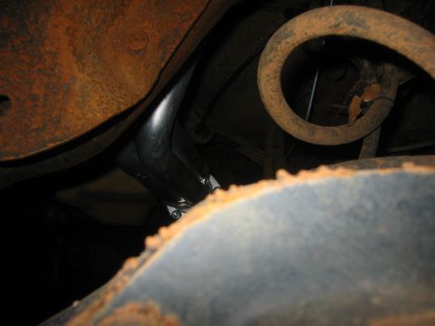 1995 Ford Bronco - The underside of a vehicle reveals rusty suspension components and a black exhaust pipe.