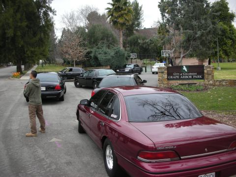 1992 Ford Crown Victoria - A maroon 1992 Ford Crown Victoria LX is parked in a lot with other vehicles, near a sign for Grape Arbor Park.
