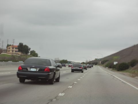 1992 Ford Crown Victoria - A black sedan, identified as a 1992 Ford Crown Victoria, travels down a highway with other vehicles.