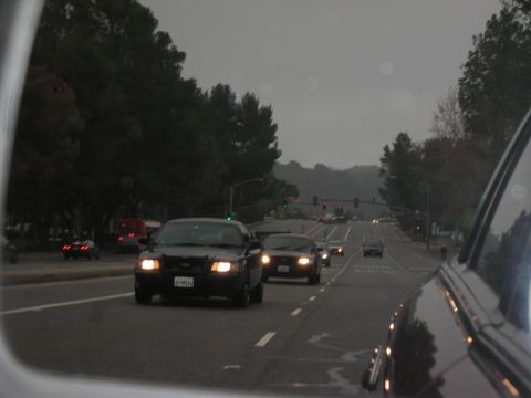 1992 Ford Crown Victoria - A police car leads traffic on a cloudy day, with other vehicles visible ahead.