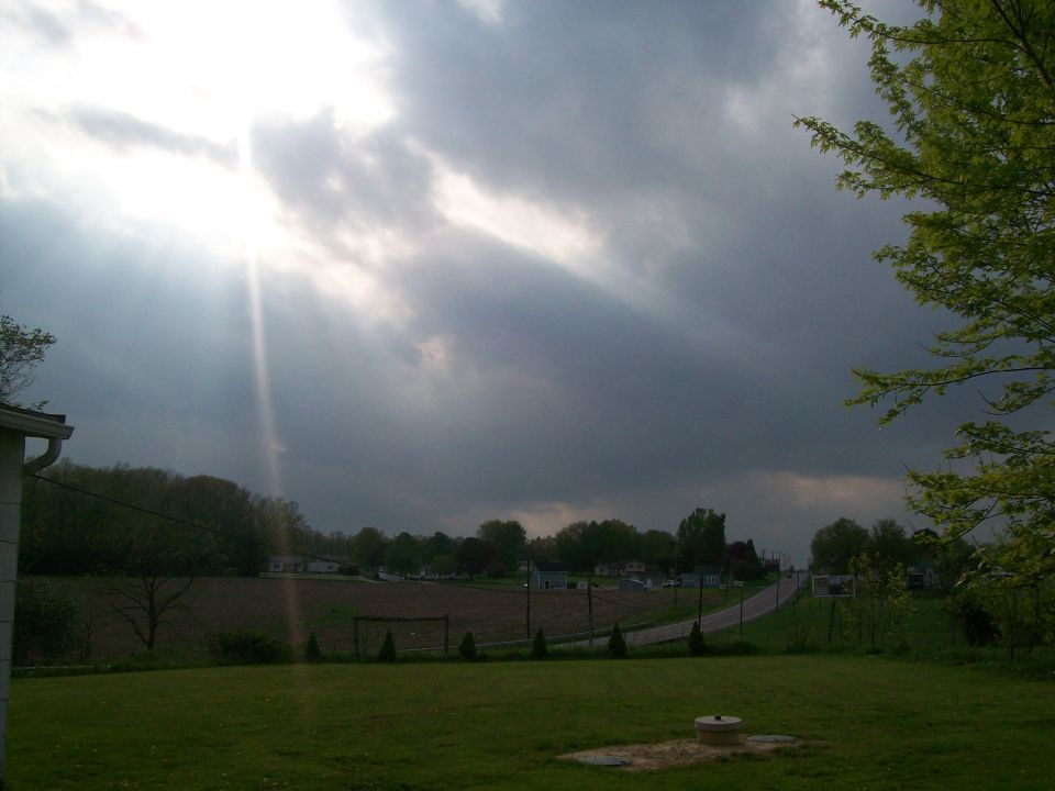 stormy sky with sunbeams over a field and road, with a house and trees visible