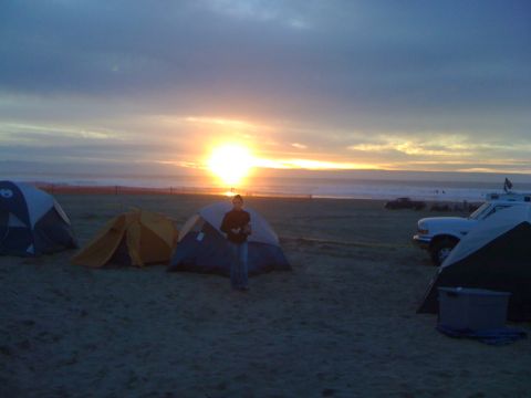 1989 Ford Bronco - Camping on the beach at sunset with multiple tents and vehicles visible.
