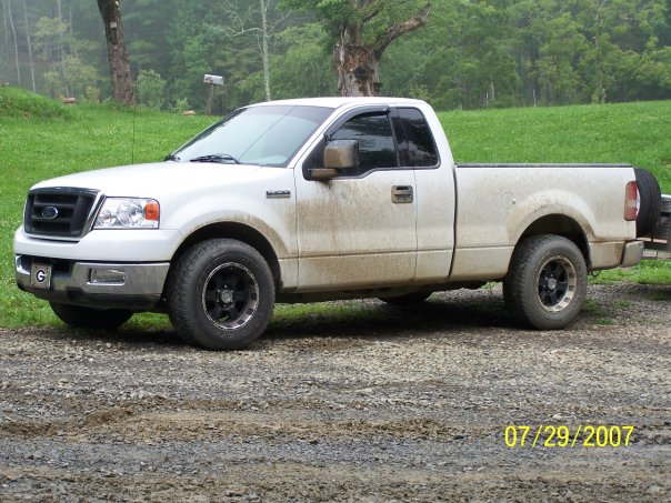 Mud-covered white Ford F-150 pickup, driver-side three-quarter view on gravel