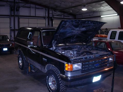 1989 Ford Bronco - 1989 Ford Bronco in a garage with its hood up, showing the engine bay.