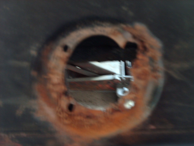 close-up of a rusted circular opening on a vehicle's undercarriage, showing some internal bracing