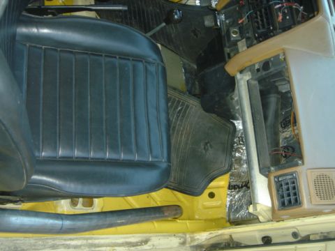 1983 Volkswagen Rabbit - The interior of a car shows black ribbed seats and exposed wiring on the dashboard, with sound-dampening material on the floor.